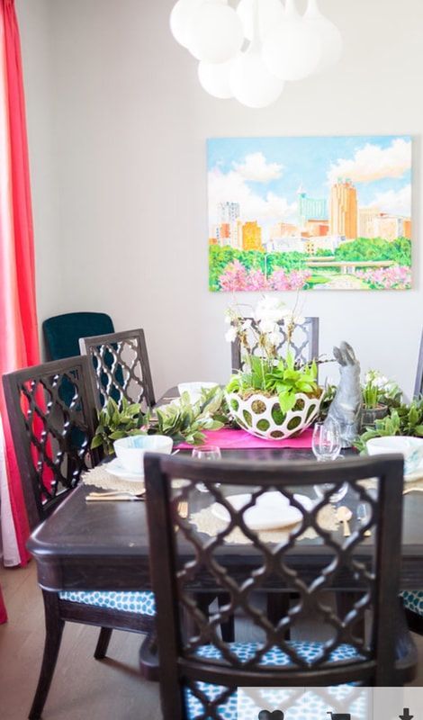 A dining room table and chairs with a painting on the wall above it.