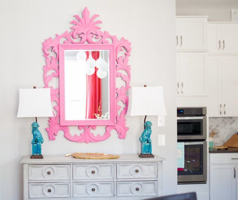 A pink mirror is above a white dresser