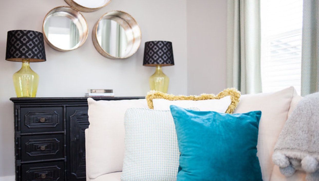 A living room with a couch , pillows , lamps and mirrors.