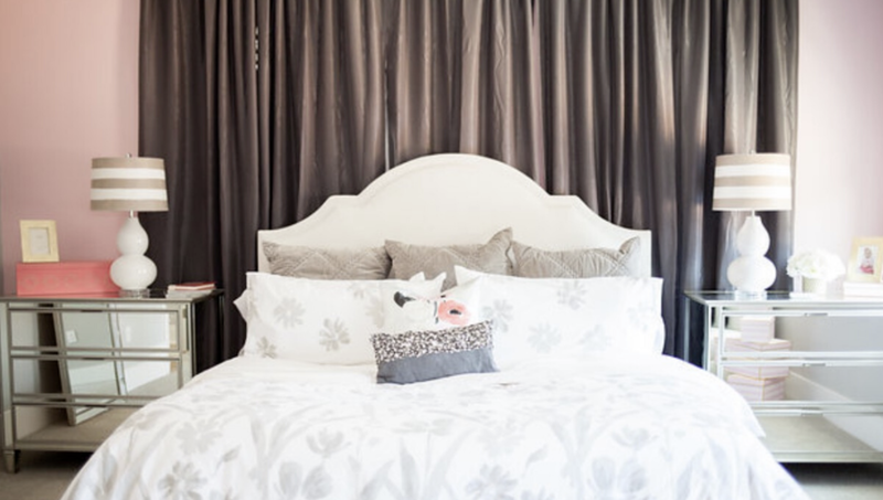 A bedroom with a bed , nightstand , lamps and curtains.