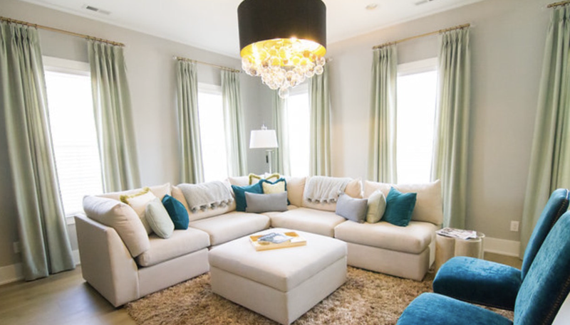 A living room with a large sectional couch , chairs , ottoman and chandelier.