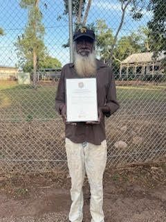 A man with a beard is holding a certificate in front of a chain link fence.