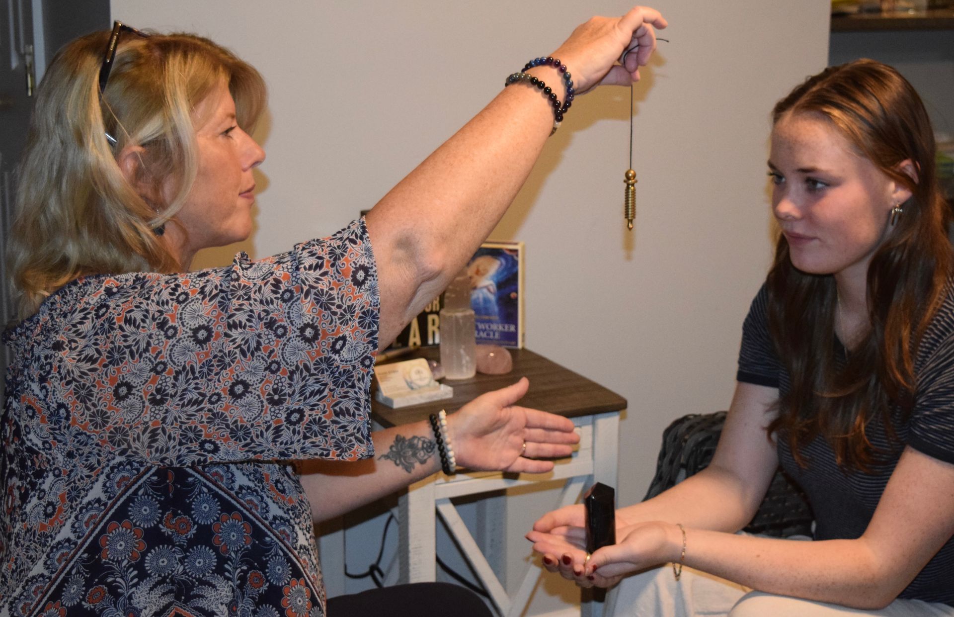 A woman is holding a pendulum over another woman 's head.