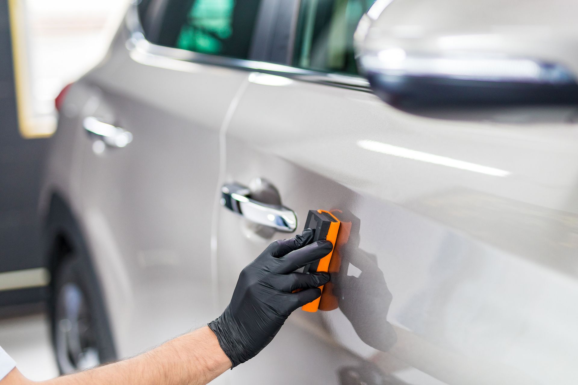 A gloved hand applies coating to a light-colored car door.