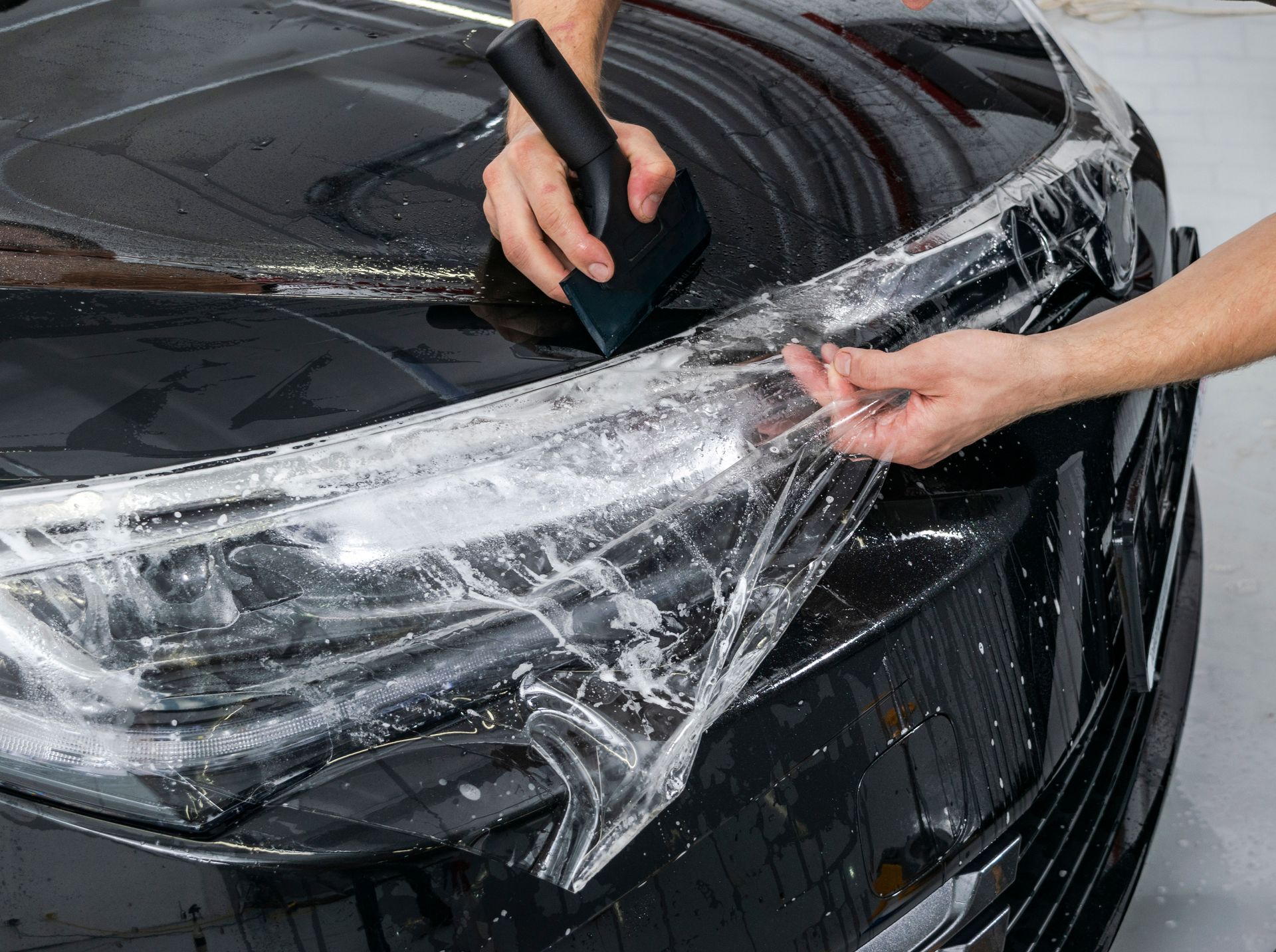 Person applying clear protective film to a car's headlight with a squeegee.