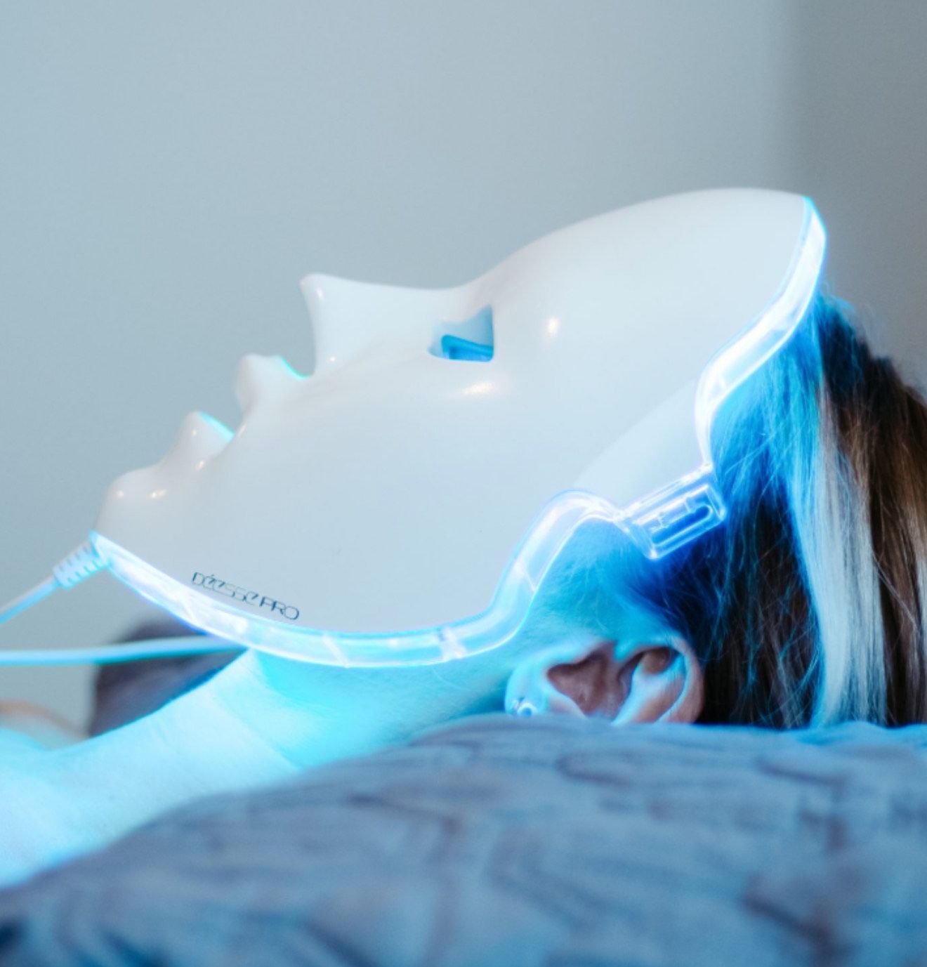 Person wearing a white LED face mask, receiving blue light therapy, lying down.
