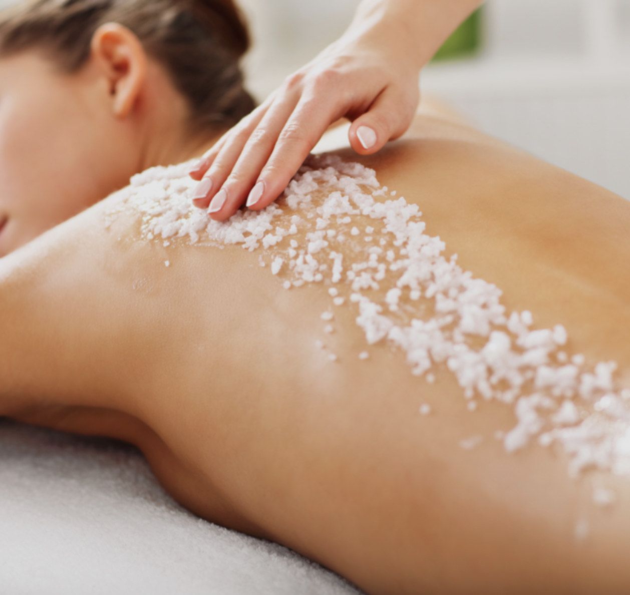 Woman receiving a body scrub massage. Therapist's hand on back, white scrub visible.