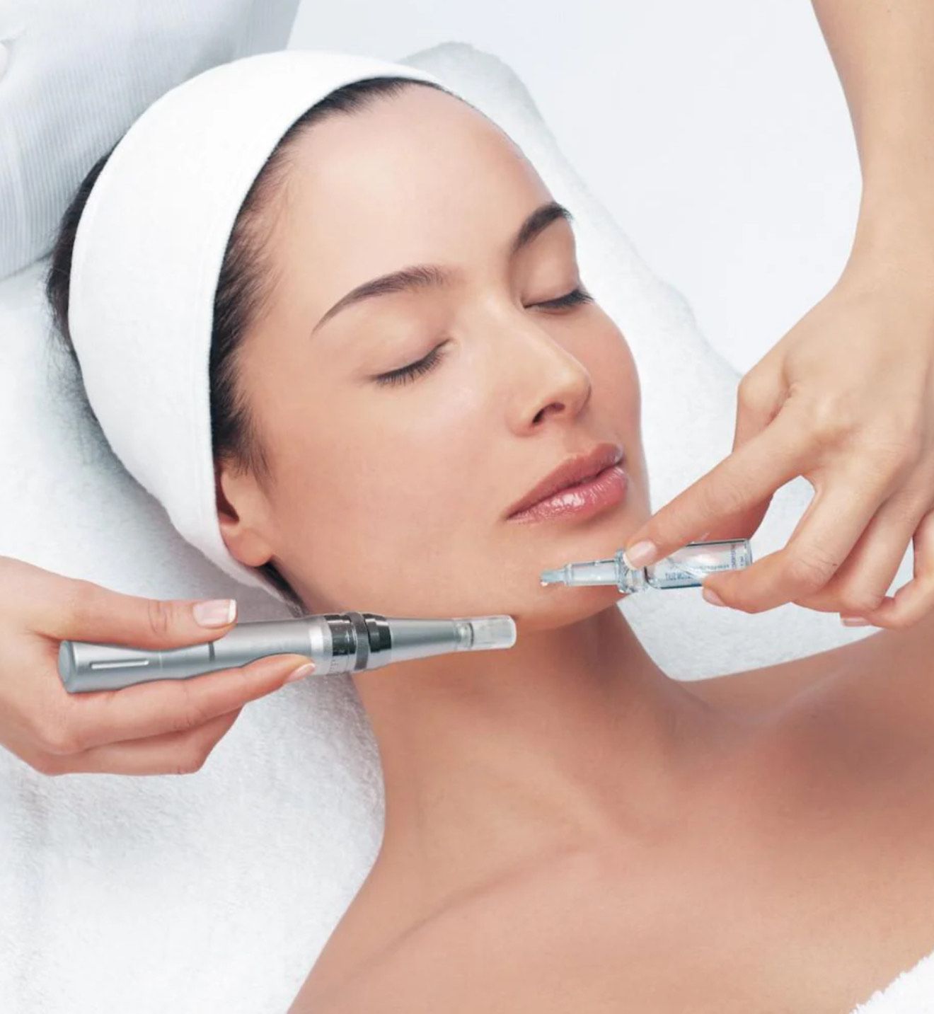 Woman receiving a facial treatment. Two hands hold syringes near her face in a spa setting.