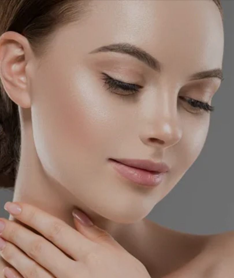Woman with flawless skin and makeup, eyes closed, hand on her neck, gray background.