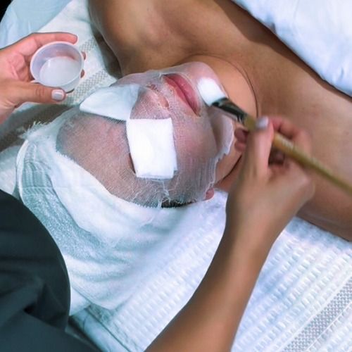 Facial treatment in progress: a person has eye and mouth protection. Someone applies product with a brush.