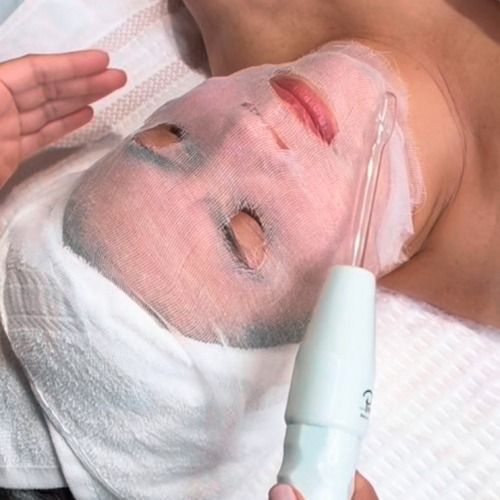 Person with a face mask receiving a facial treatment with a wand.