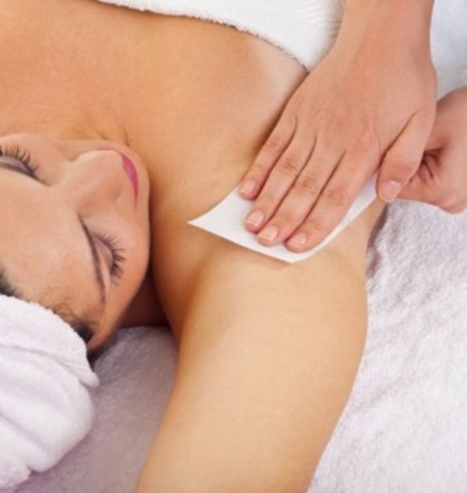 Woman getting underarm waxed; hand applies wax strip.
