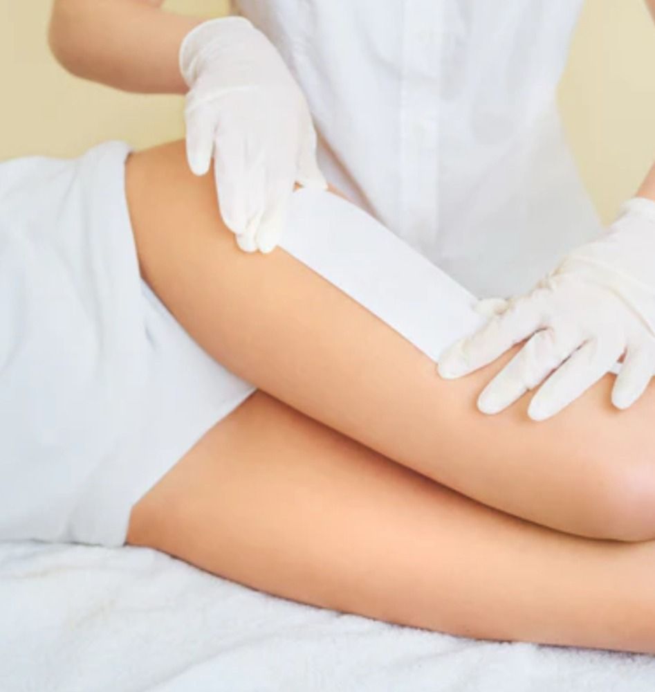 Person receiving leg waxing treatment at a spa. Technician in gloves applying wax strip.