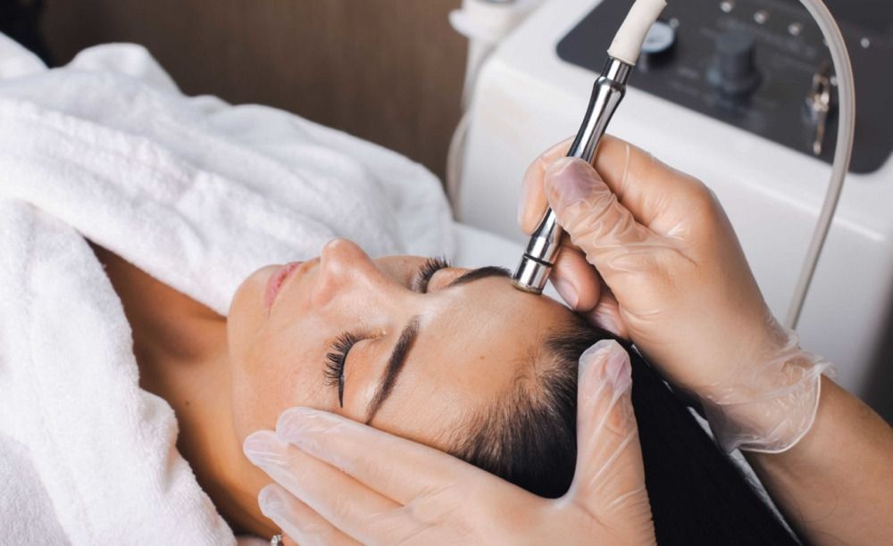 Woman receiving a facial treatment. A professional uses a skincare device on her forehead.