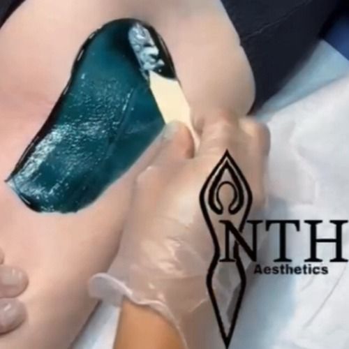 Person waxing leg with teal wax, wearing gloves. NTH Aesthetics logo present.