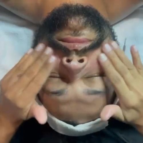 Person receiving a facial massage, eyes closed, with hands on face; indoors.
