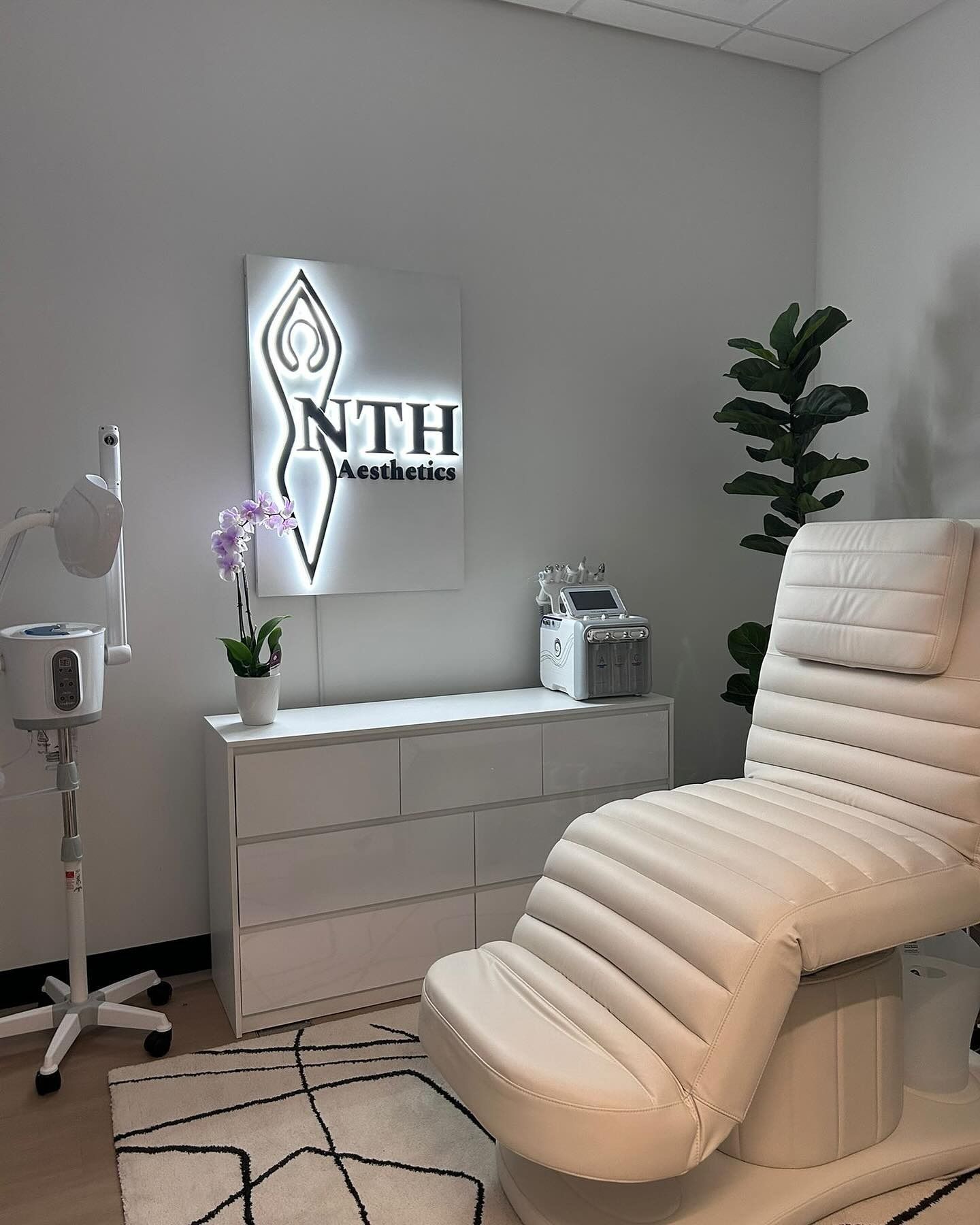 Bright white treatment room with a reclined chair, equipment, and sign.