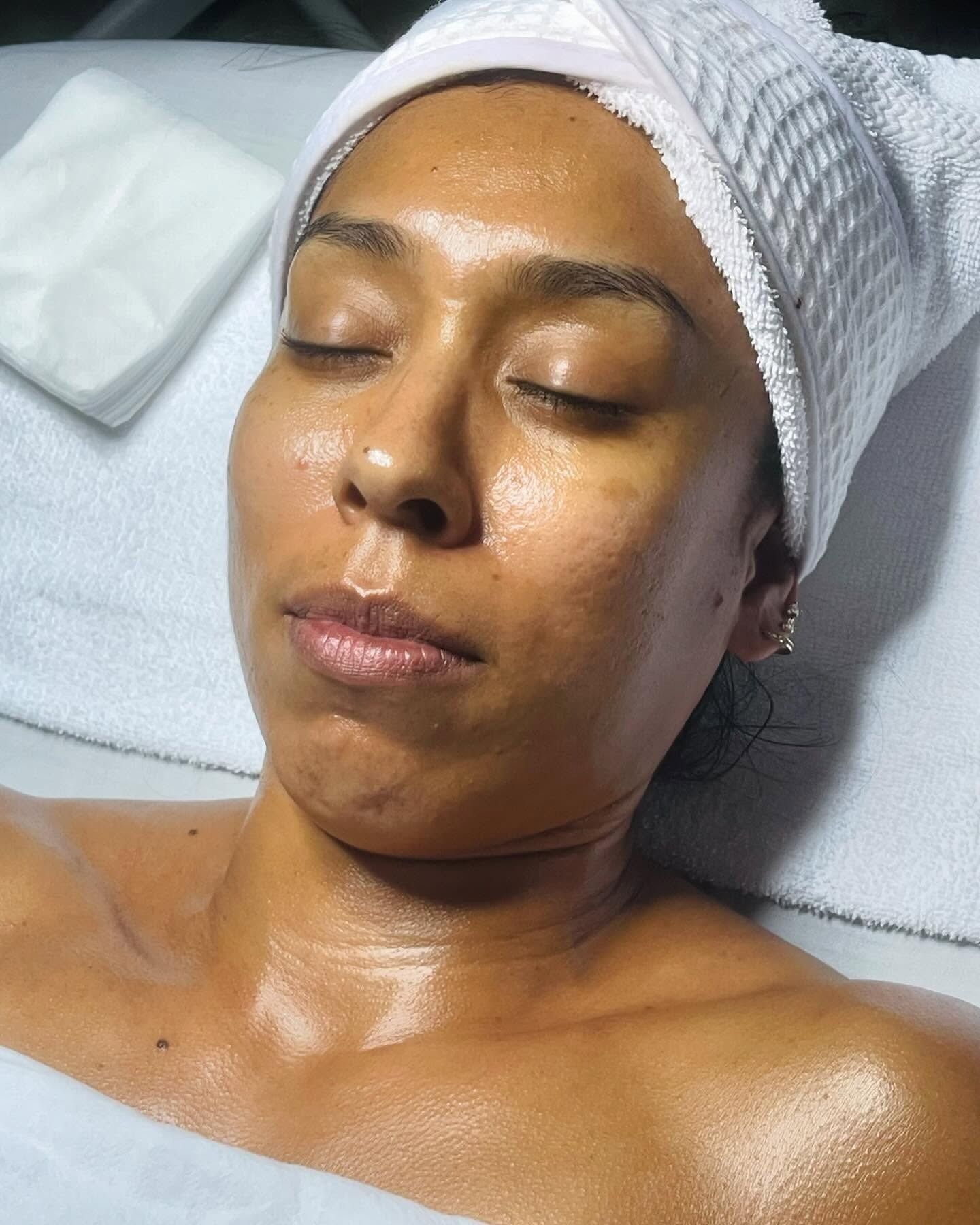 Woman with towel on head, eyes closed, skin treated with oil, on spa table.