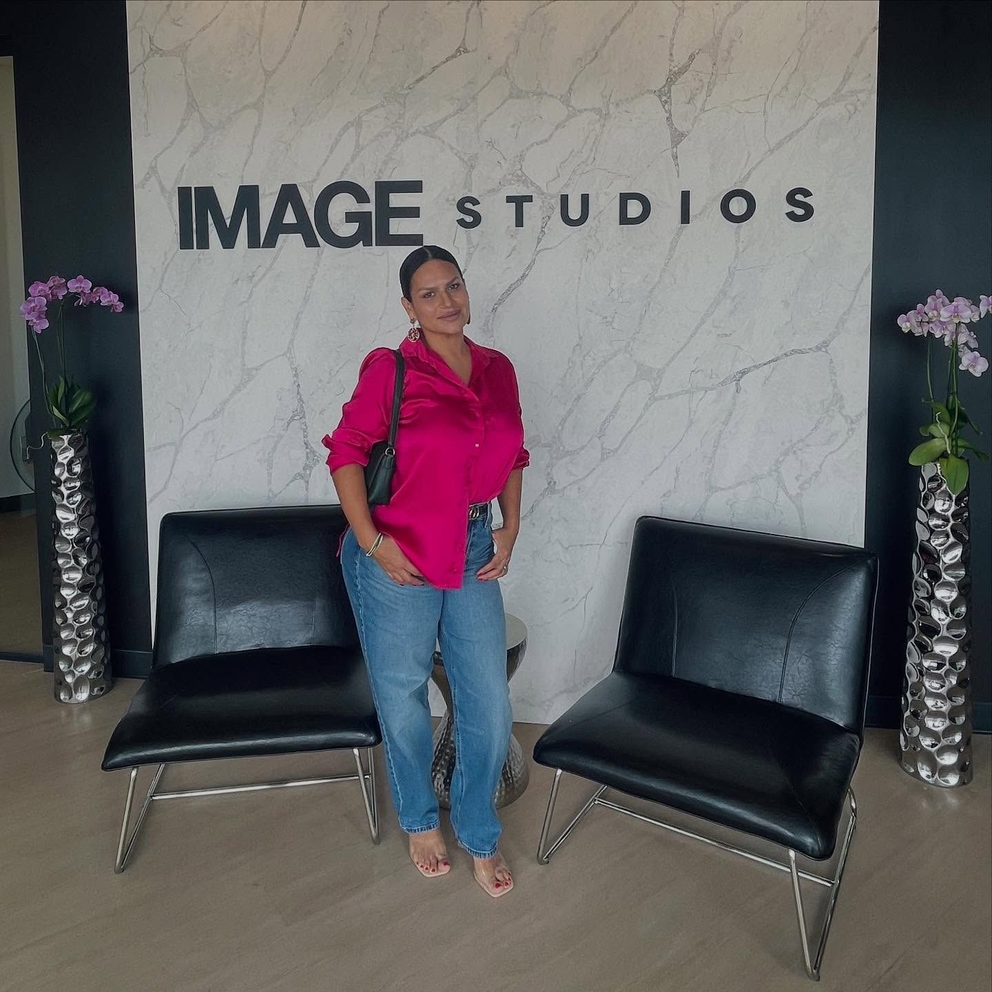Woman in pink shirt and jeans poses in front of 