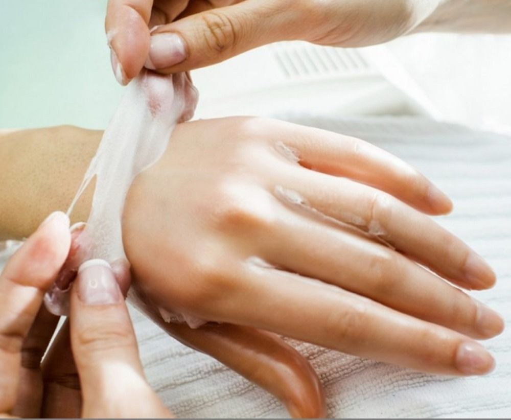 Hands receiving a paraffin wax treatment, with strips being peeled off, indoors.
