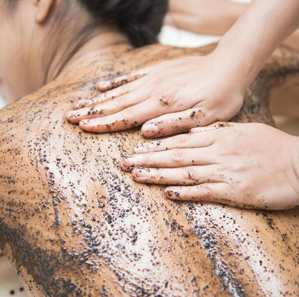 Person receiving a back scrub massage. Hands applying brown scrub to skin.