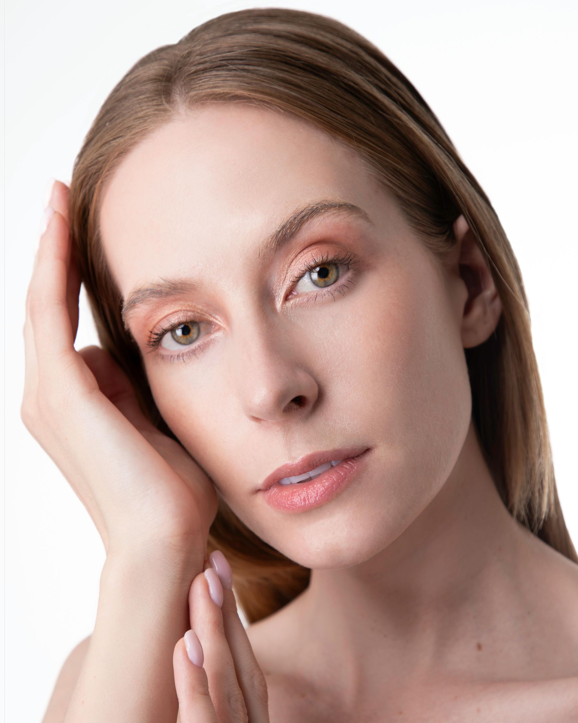 Woman with light skin and long blonde hair, posing with hand near face, soft lighting.