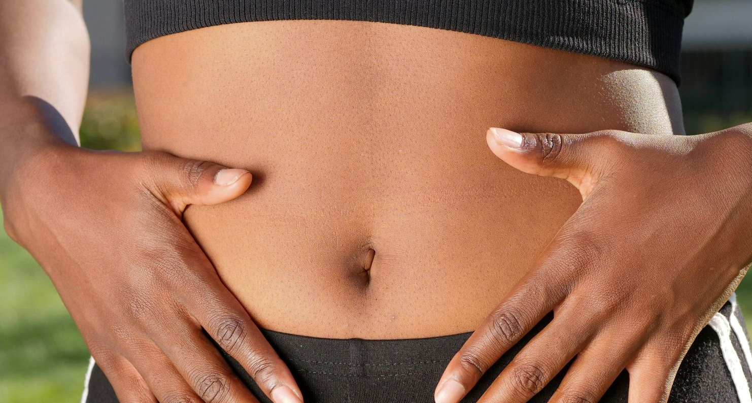 Person holding their hands near their stomach, cropped shot of abdomen. Dark skin, wearing a black top and shorts.