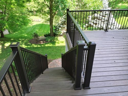 A wooden deck with stairs leading up to it and a black railing.