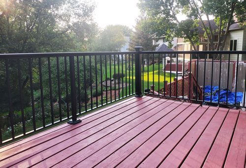 A red deck with a black railing and a view of a yard.