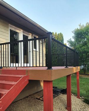 A deck with stairs and a black railing is in front of a house.