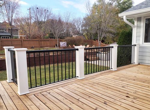 A wooden deck with a black railing and white posts in front of a house.