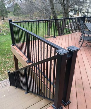 A wooden deck with a black railing and stairs leading up to it.