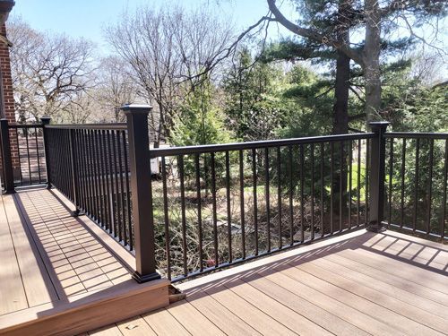 A wooden deck with a black railing and trees in the background.