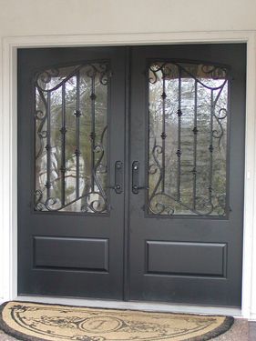 A pair of black doors with a wrought iron design and a door mat.