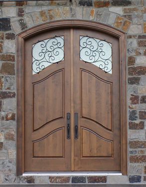 A wooden door with a wrought iron frame is on a brick wall.