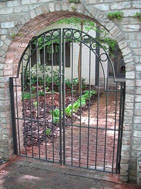 A brick archway with a wrought iron gate leading to a garden