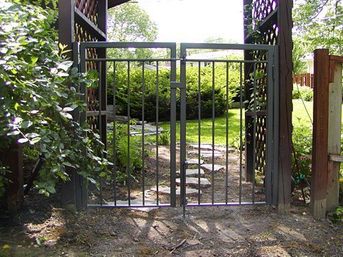 A metal gate leading to a garden with trees in the background