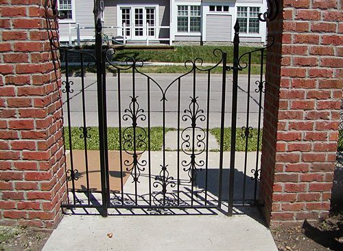 A wrought iron gate with a brick wall behind it