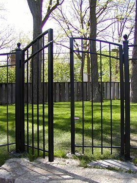 A black wrought iron gate is open to a lush green field.