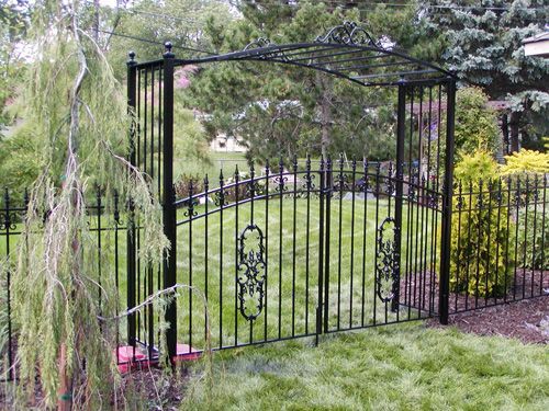 A black wrought iron gate is surrounded by a lush green lawn.