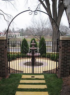 A wrought iron gate leading to a garden with a fountain