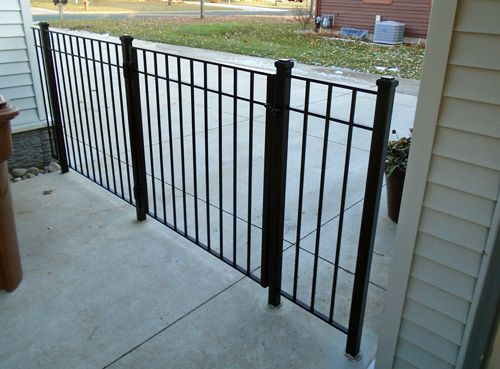 A black wrought iron fence is sitting on a patio next to a house.
