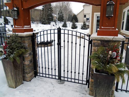 A wrought iron gate is surrounded by potted plants in the snow