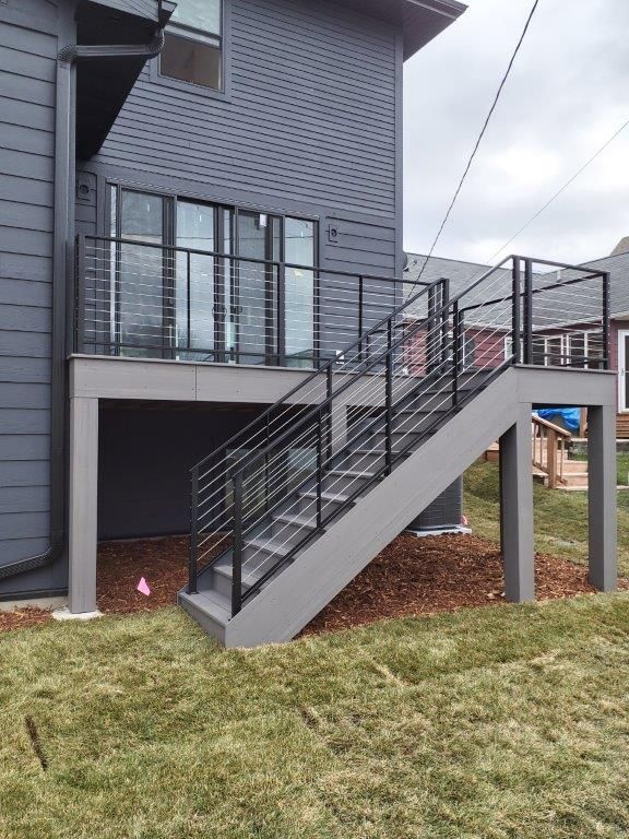 A gray deck and stairs with black railings attached to a dark gray house.