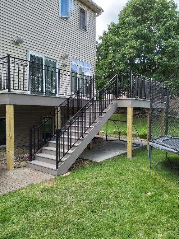 A deck with stairs and a trampoline in the backyard