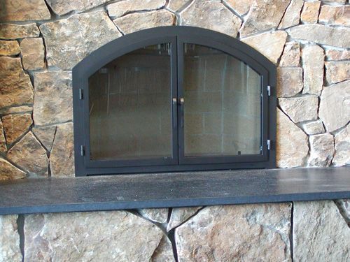 A fireplace with a black door and a stone wall behind it.