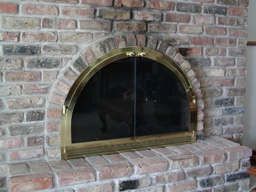 A brick fireplace with a brass door and a glass screen.