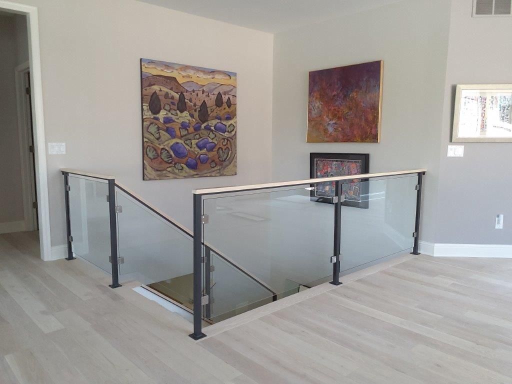 A staircase with a glass railing and a painting on the wall.