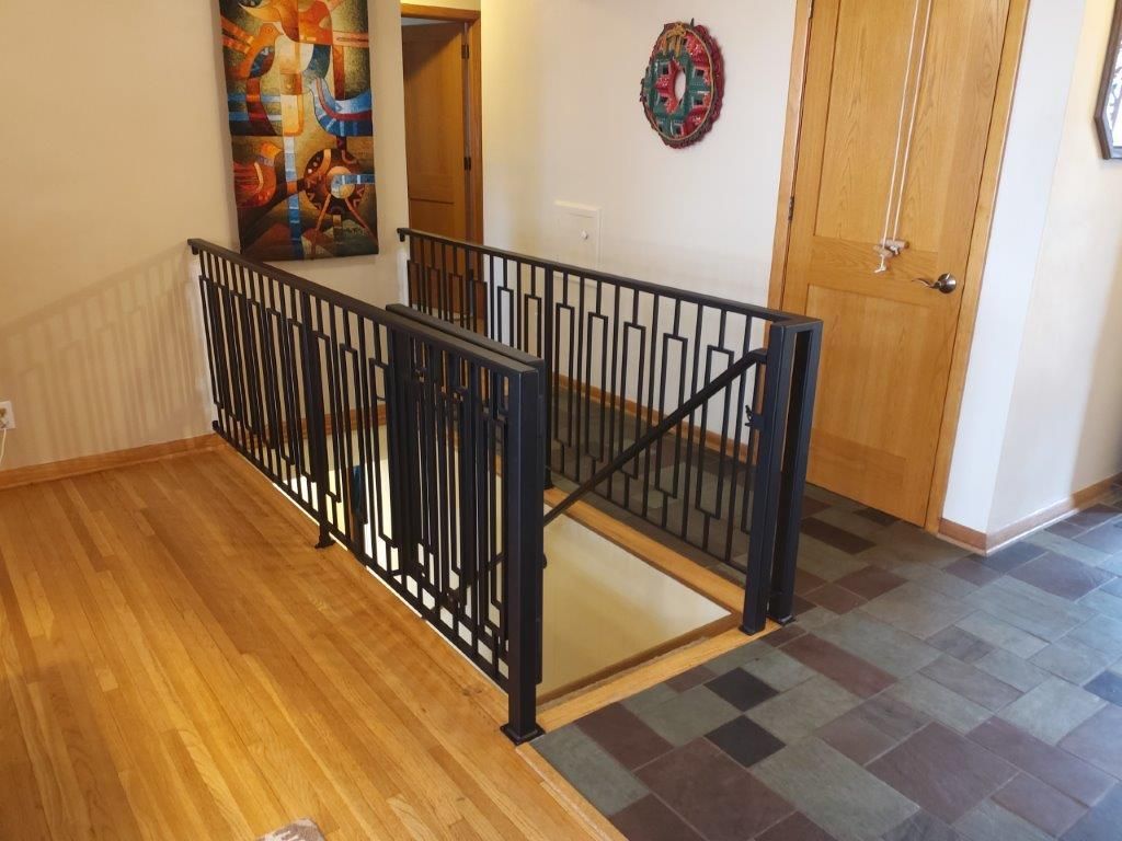 Hallway with metal railing leading to lower level, wood floors, and artwork on the wall.