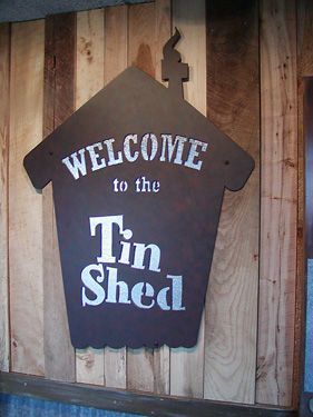 A sign on a wooden wall that says welcome to the tin shed